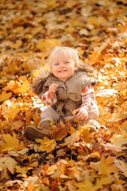 Little cute girl is sitting in a pile of leaves. Autumn season.