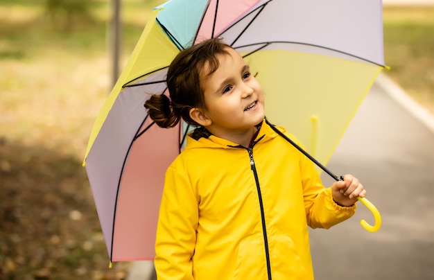 Little cute girl kid child in a yellow raincoat with multicolored rainbow umbrella laughs