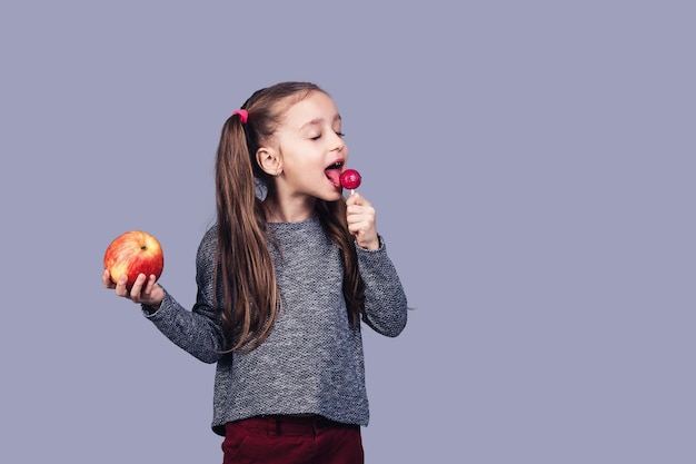 Little cute girl licks a lollipop and holds an apple