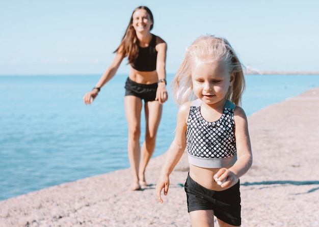 Little cute girl looking to the fit mom on the beach