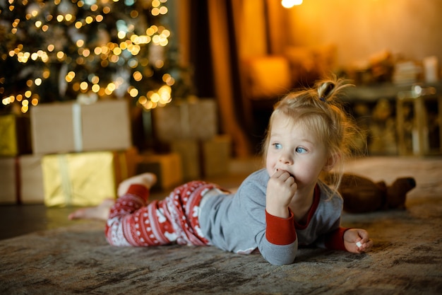 Little cute girl lying on the carpet in pyjamas waiting for Christmas.