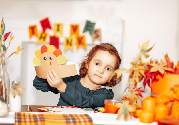 Little cute girl made paper turkey hat for celebrating Thanksgiving day Diy craft art project