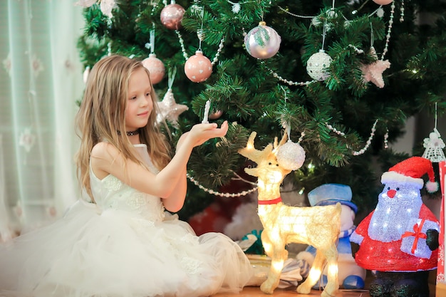 Little cute girl near christmas tree. Children under Christmas tree with gift boxes.