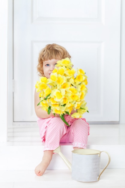 Little cute girl in pink dress sitting on white porch and hides her face behind bouquet of flowers ,