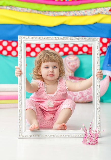 Little cute girl in a pink suit sitting on the floor and smiling over wooden white frame.