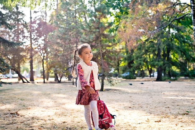 a little cute girl in a red dress a schoolgirl walks in an autumn park with a backpack