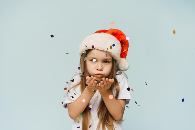 Little cute girl in santa hat blows confetti into the camera Christmas and New Year