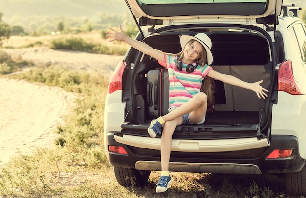 Little cute girl in the trunk of a car with suitcases