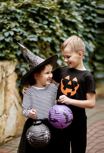 Little cute girl in witch costume and boy holding paper lanterns Kids having fun on Halloween holiday