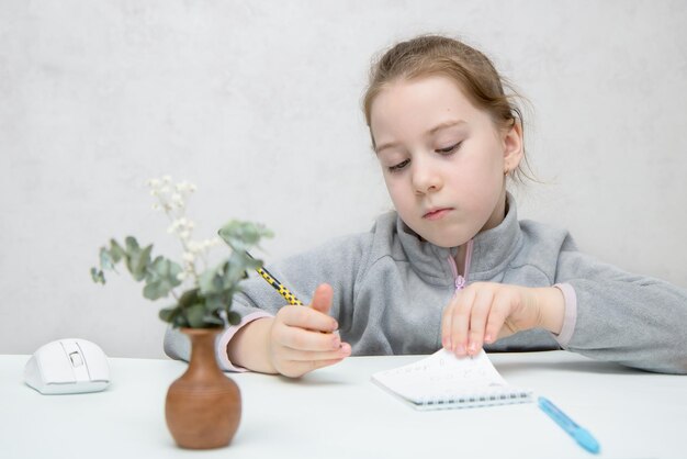 Little cute girl writes intently in a notebook at the table