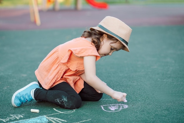 Little cute happy girl draws painting a chalk on pavement asphalt on ground on playground Creative children summer activity