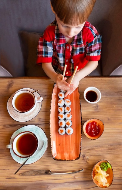 Little cute little boy eating sushi in a cafe concept of eating top view of child eating sushi with chopsticks