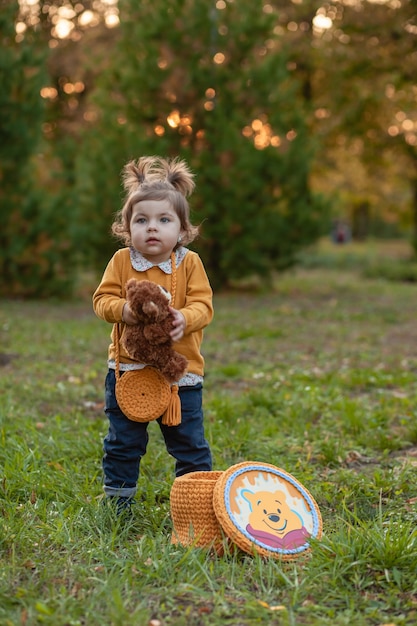 Little cute sad girl holding in hands brown teddy bear, upset child spending time outdoors in spring time