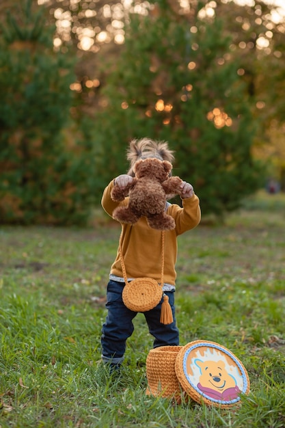 Little cute sad girl holding in hands brown teddy bear, upset child spending time outdoors in spring time