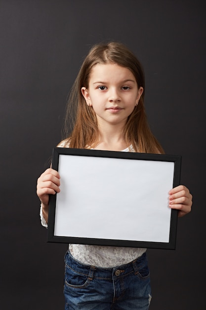 Little dark hair girl posing with frame in studio on black background