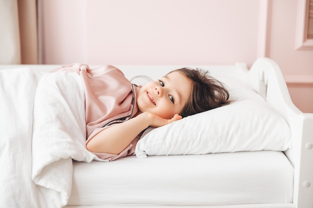 A little darkhaired girl lying barefoot in bed the child woke up after sleeping good morning