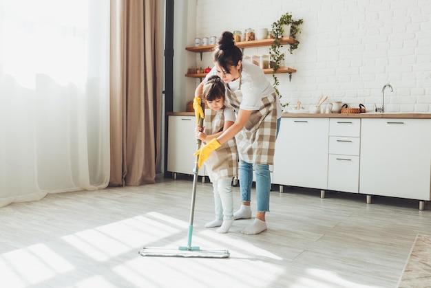 A little daughter and her mom clean the house a child washes the kitchen floor a cute little helper girl cleans the floor with a mop a happy family cleans the room