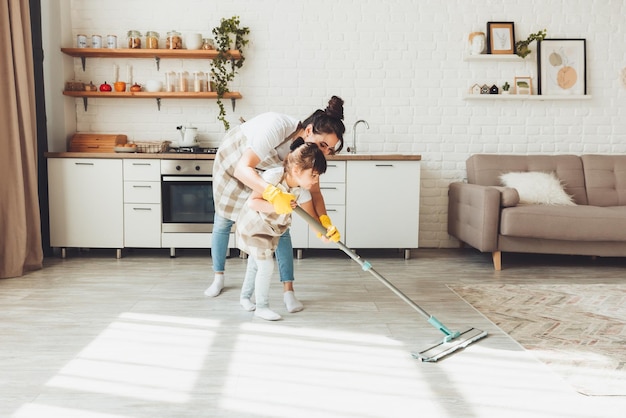 A little daughter and her mom clean the house a child washes the kitchen floor a cute little helper girl cleans the floor with a mop a happy family cleans the room