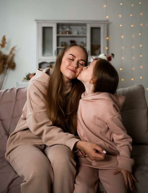 A little daughter is sitting on the couch and kissing her mother