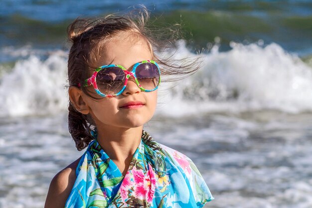 Little dreamy girl with closed eyes in sunglasses in which the sun is reflected at sea