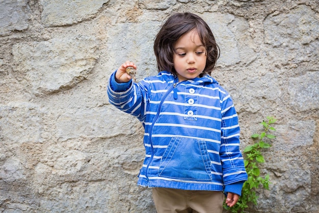 Little eastern handsome baby boy playing outdoor with a snail