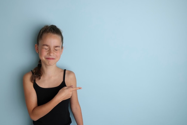 Little emotional teenage girl in a black tshirt 11 12 years old on an isolated blue background Children39s studio portrait Place the text to copy the place for the inscription