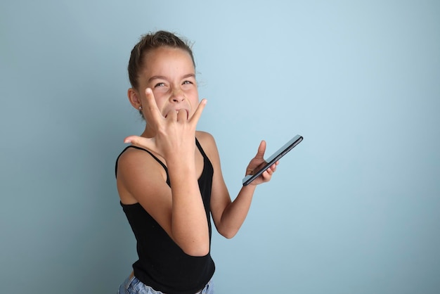 Little emotional teenage girl in pink shirt 11 12 years old on an isolated blue background with a tablet in her handsChildren39s studio portrait Place the text to copy the place for the inscription