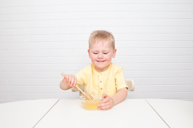 Little European boy with blue eyes is tasting honey