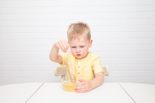 Little European boy with blue eyes is tasting honey