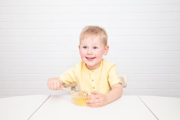 Little European boy with blue eyes is tasting honey