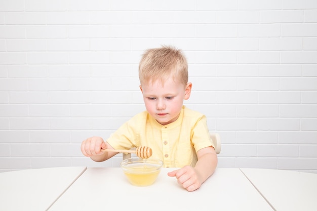 Little European boy with blue eyes is tasting honey