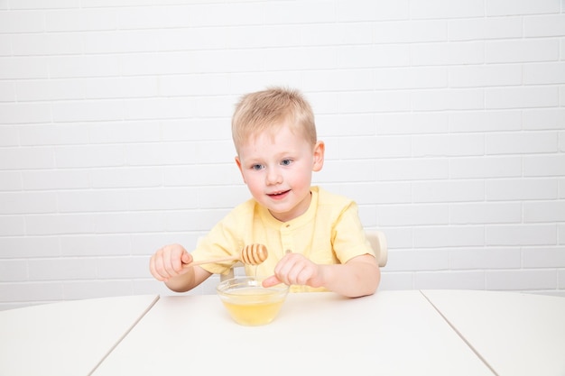 Little European boy with blue eyes is tasting honey