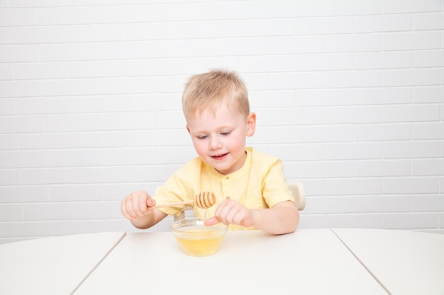 Little European boy with blue eyes is tasting honey