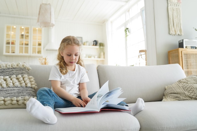 Little european girl with book has leisure at cozy home Preschool child is learning to read