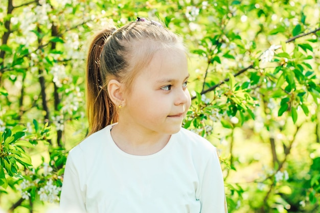 Little fairhaired girl on the background of flowering trees