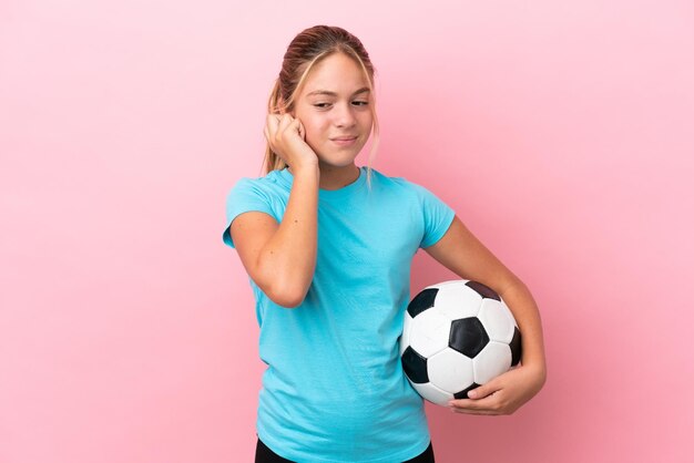 Little football player girl isolated on pink background frustrated and covering ears