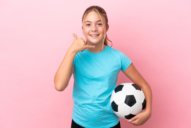 Little football player girl isolated on pink background making phone gesture. Call me back sign