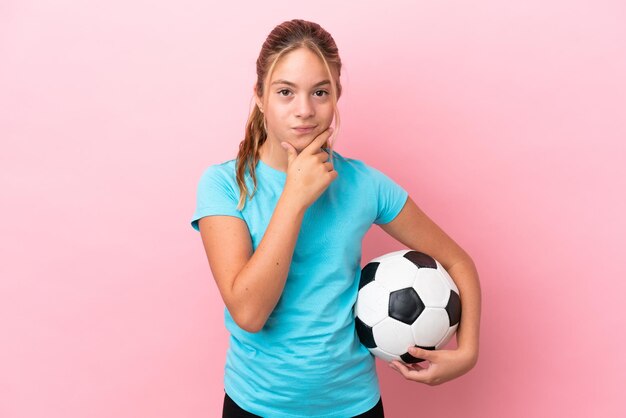 Little football player girl isolated on pink background thinking