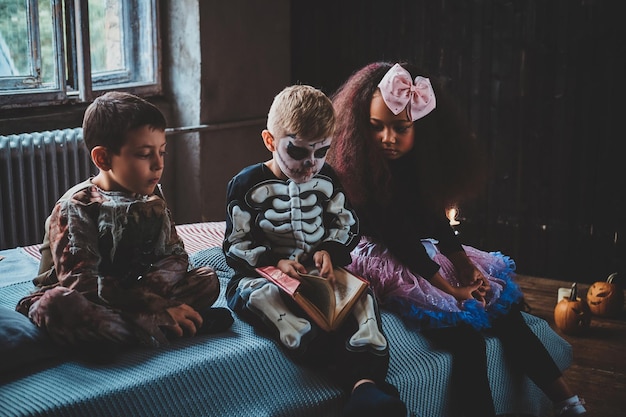 Little friends are waiting for Halloween party while reading book and sitting on bed.