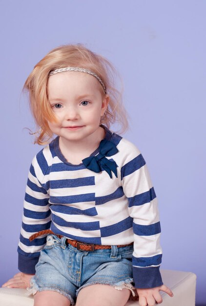 Little funny blonde girl wear striped shier and denim shorts over blue in room