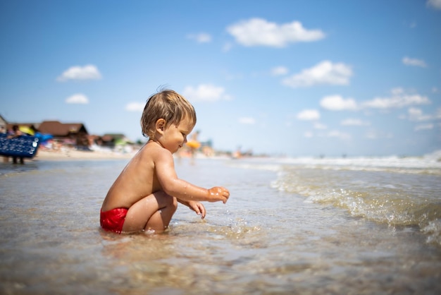 Little funny funny kid collects shells and pebbles in the calm blue sea on a sandy bottom under the hot summer sun on a bright vacation