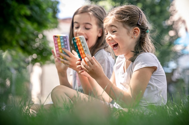 Little funny girls outdoors with phones in a case with pimples pop it, a trendy anti stress toy.