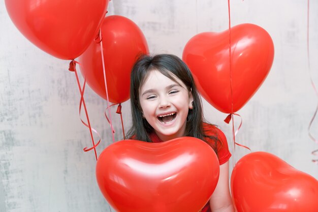 little funny laughing girl face close up among red heart-shaped balloons