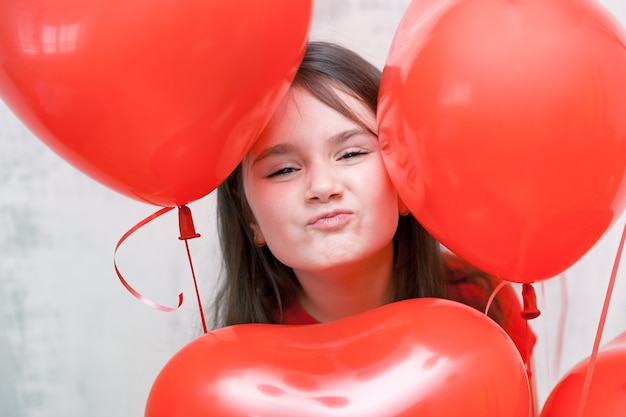 little funny naughty girl face close up among red heart-shaped balloons