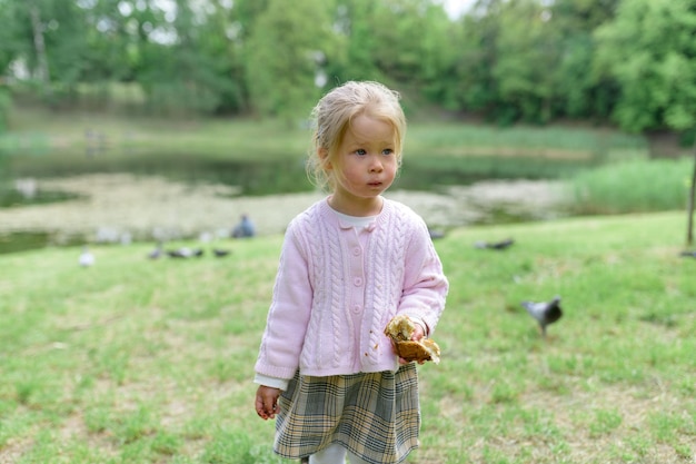 A little girl 2 years old with pouting lips holds a bun in her hand