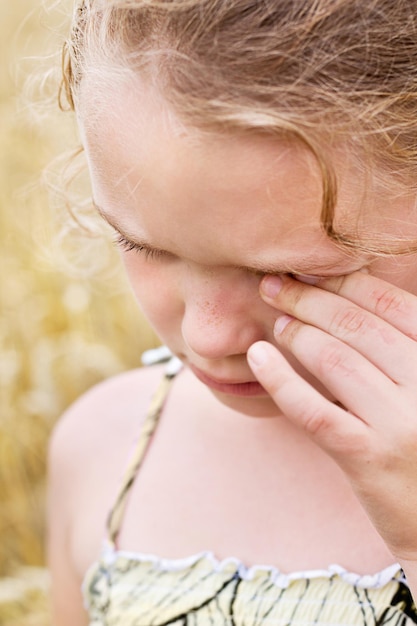 Little girl are crying and rubs her eye with her hand, allergy for blooming plants.