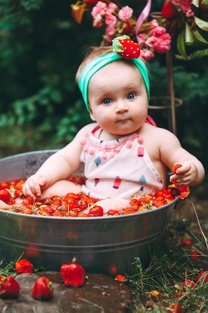 A little girl bathes in a basin with strawberries in the garden.