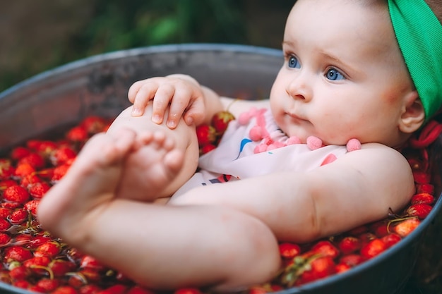 A little girl bathes in a basin with strawberries in the garden.