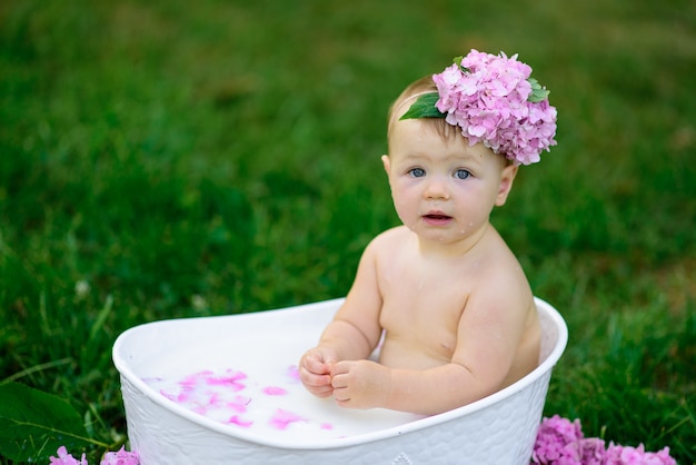 Little girl bathes in a milk bath in the park. The girl is having fun in the summer.