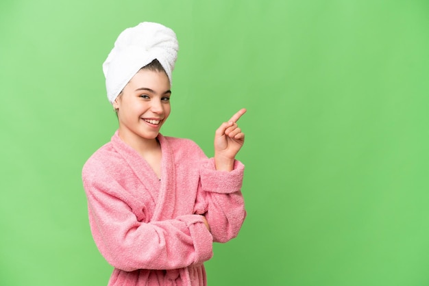 Little girl in a bathrobe over isolated chroma key background pointing finger to the side